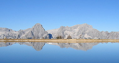 zeigt den Höss-See mit Spiegelung der Prielgruppe